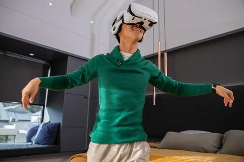 White VR headset is resting on low bed near window seat in modern bedroom Stock Photos