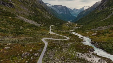 White VW camper van driving through dramatic mountain valley beside river in Vídeos de archivo 331978451