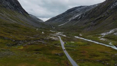 White VW camper van driving through dramatic mountain valley beside river in Vídeos de archivo 331978498