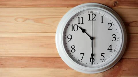 White wall clock showing half past ten on a wooden background. Stock Photos