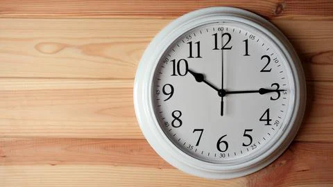 White wall clock showing quarter past ten on a wooden background. Stock Photos