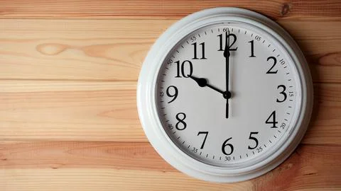 White wall clock showing ten o clock on a wooden background. Stock Photos