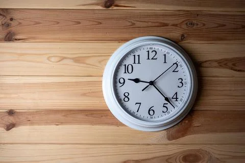 White wall clock showing time on a wooden panel background. Stock Photos