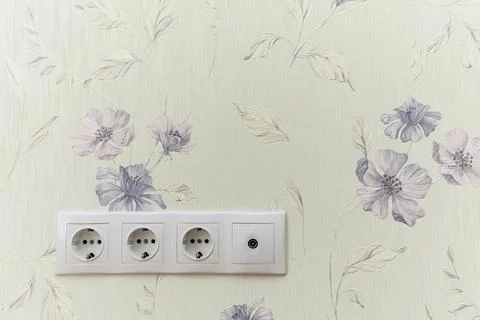 A white wall with a floral pattern and a white electrical outlet Stock Photos