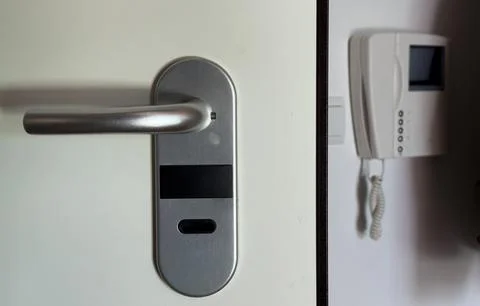 A white wall with an intercom hanging on the wall, a light-on button and an.. Stock Photos
