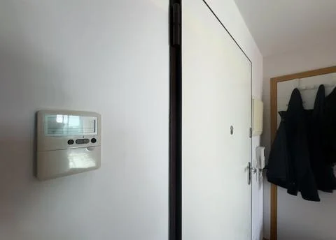 A white wall with an intercom hanging on the wall, a light-on button and an.. Stock Photos