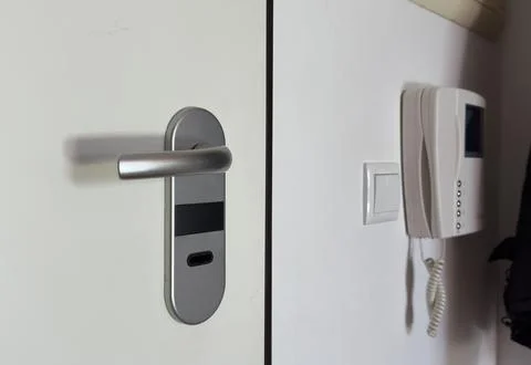 A white wall with an intercom hanging on the wall, a light-on button and an.. Stock Photos
