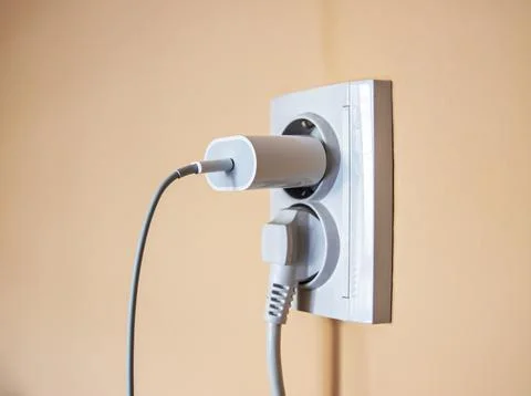 White wall socket with a connected power adapter and a thick power cord, el.. Stock-Fotos