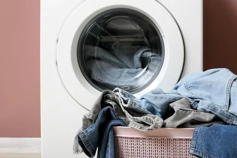 White washing machine with a full load of denim jeans and a laundry basket of Stock Photos