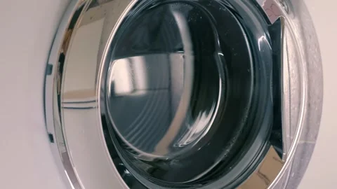 White washing machine with shiny chrome door washes clothes according to program Stock Footage 297772155