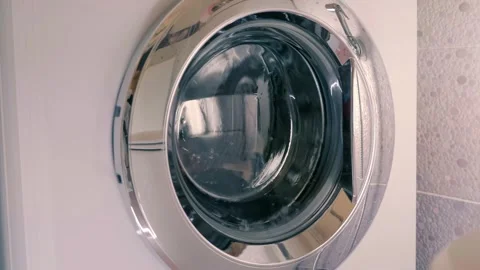 White washing machine with shiny chrome door washes clothes according to program Stock Footage 297792376
