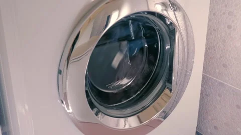 White washing machine with shiny chrome door washes clothes according to program Stock Footage 297792764
