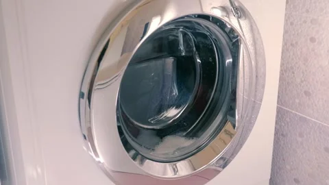 White washing machine with shiny chrome door washes clothes according to program Stock Footage 297824733