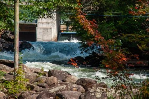 White water rapids flow under a sturdy cement bridge with a dam Stock-Fotos