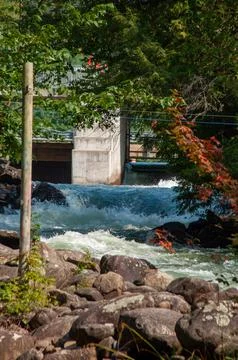 White water rapids flow under a sturdy cement bridge with a dam Stock Photos