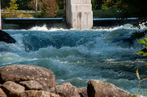 White water rapids flow under a sturdy cement bridge with a dam Stock Photos