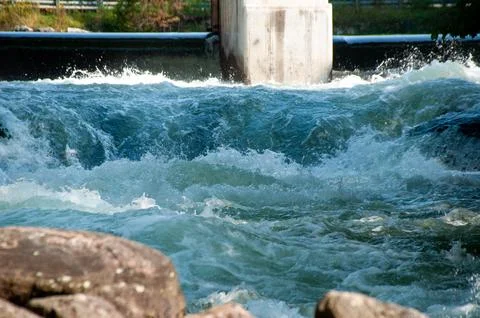 White water rapids flow under a sturdy cement bridge with a dam Stock Photos