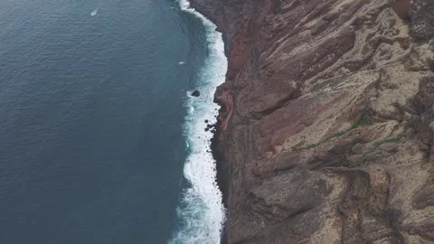 White waves powerfully surging against volcanic dark cliffs, revealing dramatic Stock Footage 308403860