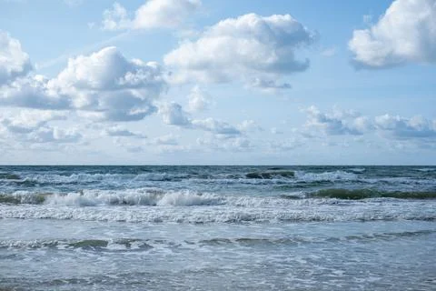 White waves of the sea with clouds in blue sky. The rolling sea on a cloudy d Stock Photos