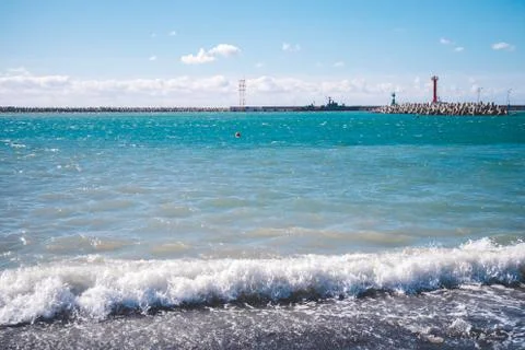 White waves, turquoise sea, bright blue sky, red lighthouse Stock Photos