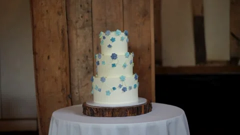 White wedding cake with blue decorative flowers, sitting on a wood slice Stock Footage 293809213