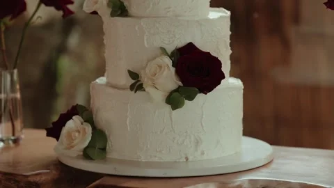 White Wedding Cake with Red and Ivory Roses and Eucalyptus on a Wooden Table Stock Footage 338437224