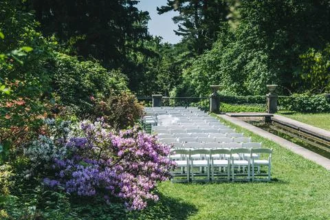 White Wedding Chairs Lined Up before a Real Life Outdoor Summer Wedding Ceremony Stock Photos