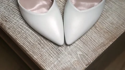 White wedding shoes are placed neatly on a wooden surface, awaiting their moment Stock Footage 317394544