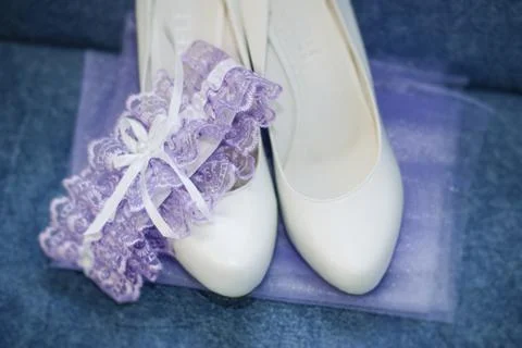 White wedding shoes for the bride and a purple garter on a blue background Stock Photos