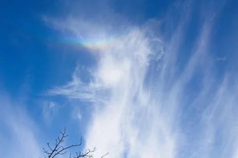 White, whispy clouds in a blue sky. A rainbow is in part of the cloud. Stock Photos