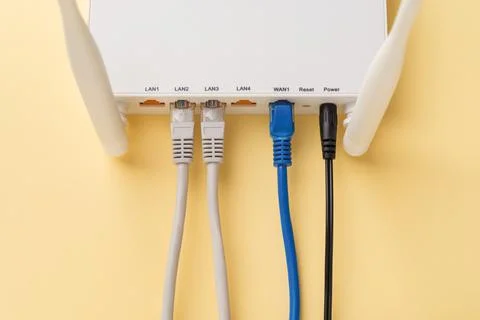 White Wi-Fi wireless router with connected network and power cables on a yellow. Stock Photos