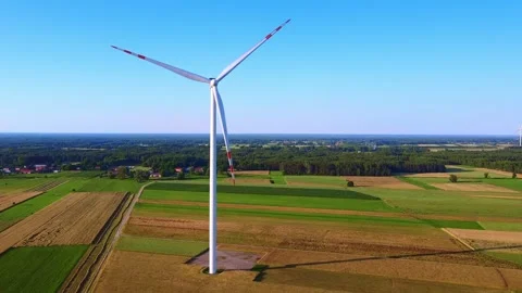 White wind turbine rotating over rural farmland during daytime Video stock 342593063