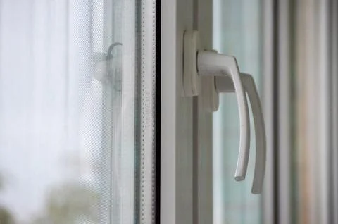 A white window handle is shown with a mesh screen in the background. Stock Photos