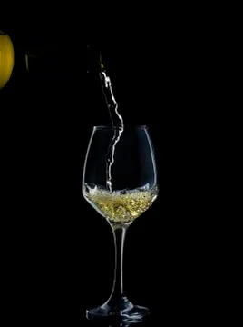 White wine is poured down into wine glass in black background Stock Photos
