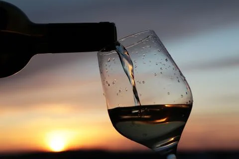 White wine pouring from a bottle into the glass on sunset background Stock Photos