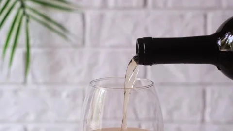 White wine pours from the neck of a bottle into a glass on a light background. Stock Footage 248781273