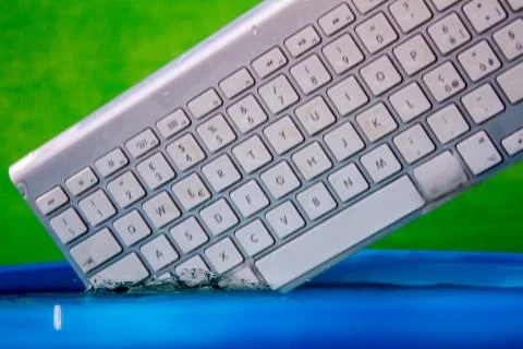 White wireless computer keyboard falling into the water spraying Stock Photos