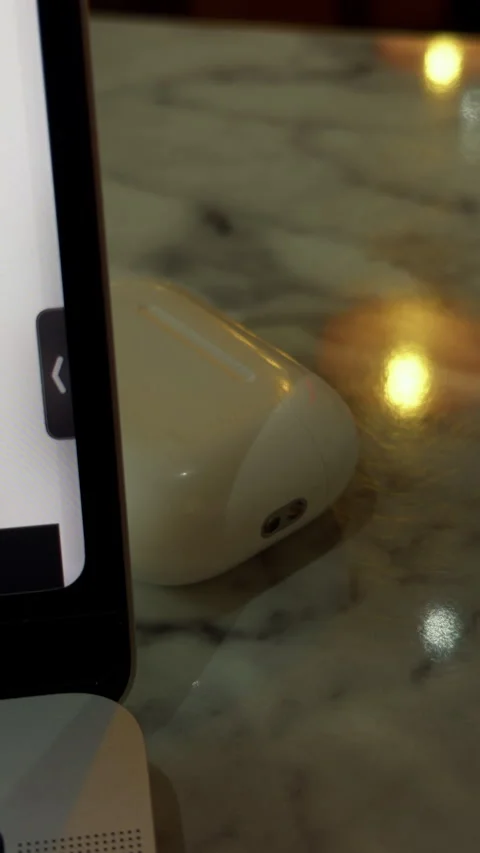 White wireless earbud beside smartphone on glossy marble tabletop with warm Stock Footage 344966202