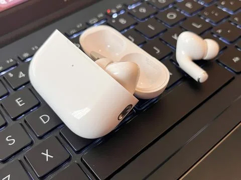 White Wireless Earbuds with Charging Case on a Backlit Laptop Keyboard Stock Photos