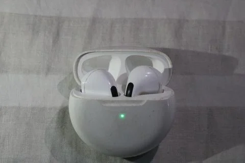 White wireless earbuds in charging case with green light on fabric background 스톡 사진