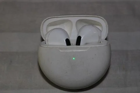 White wireless earbuds in open charging case with green light on gray surfa.. Fotos Stock