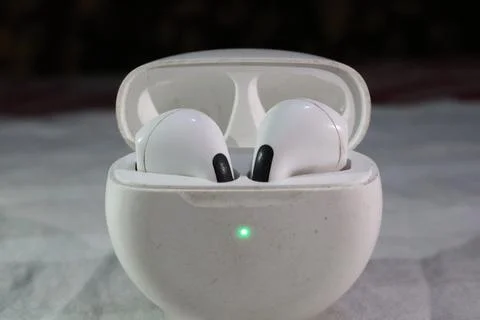 White wireless earbuds in open charging case with green light on gray surface Fotos Stock