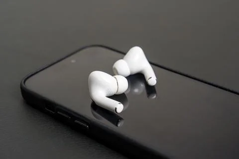 White wireless earbuds rest on black smartphone Stock Photos