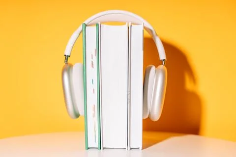 White wireless headphones on a stack of books in front of a yellow background Stock Photos