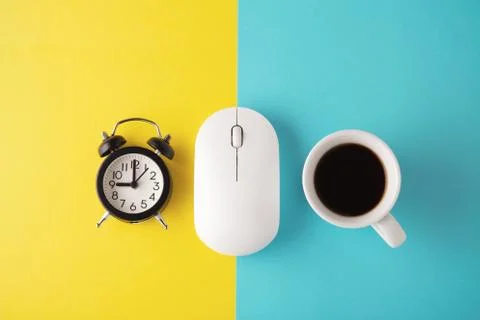 White wireless mouse with clock and coffee cup on yellow blue background, min Stock Photos