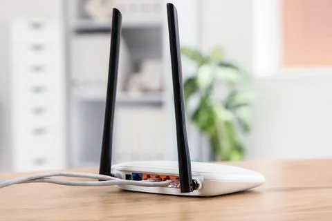 White wireless router with two antennas and connected cables on a wooden desk Stock Photos