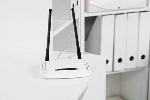 White wireless router with two black antennas on a desk in a modern office se Stock Photos