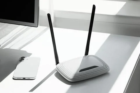 White wireless wi-fi router with two antennas and a smartphone on a desk, int Stock Photos