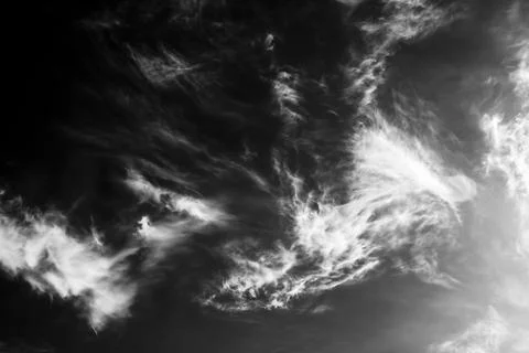 White wispy clouds drift across a dark black sky in this high contrast Stock Photos