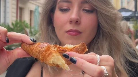 White woman eats piece from crispy croissant in city street cafe Video stock 282106714